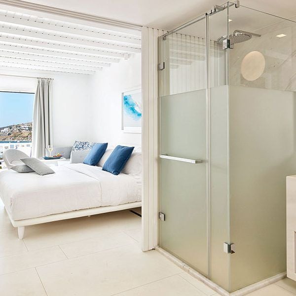 Luxurious white minimalist hotel room with panoramic sea view, elegant design, crisp linens, and modern Cycladic architecture at Myconian Ambassador Hotel, Mykonos.