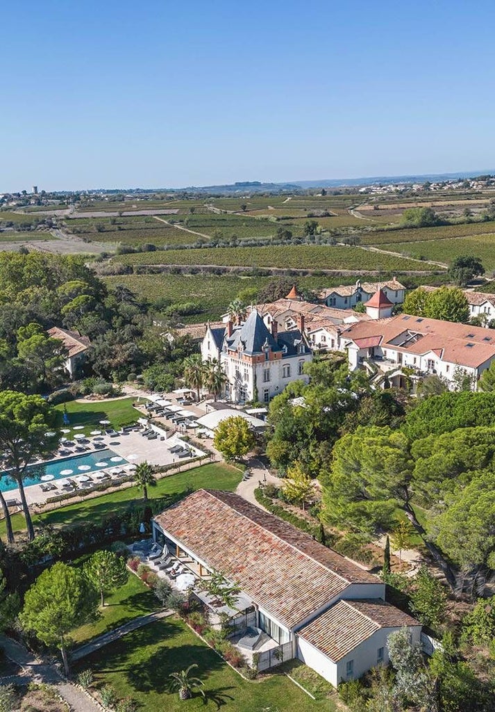 Elegant limestone château nestled in Languedoc vineyards, featuring sun-drenched stone facade, manicured gardens, and rolling lavender-lined countryside in southern France