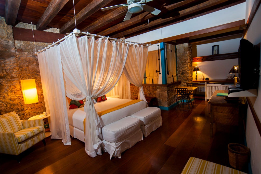 Elegant yellow-themed luxury suite with plush white bedding, decorative turquoise accents, and warm wooden furnishings in Brazilian boutique hotel