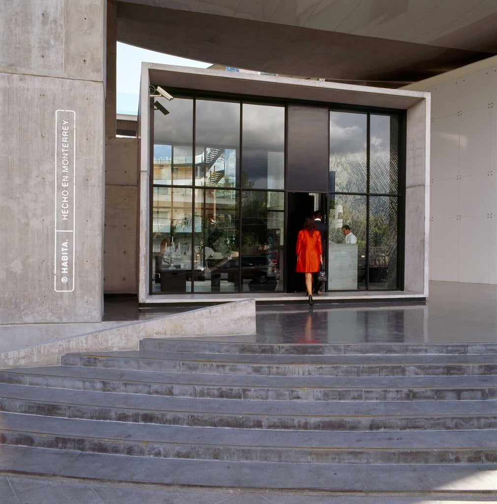 Modern glass-and-steel boutique hotel with minimalist design overlooking Monterrey cityscape, featuring sleek architectural lines and urban contemporary aesthetic at sunset