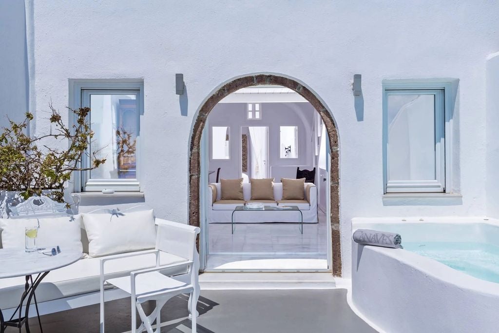 Whitewashed luxury hotel suites cascade down Santorini's cliffside, featuring private infinity pools overlooking the Aegean Sea at sunset