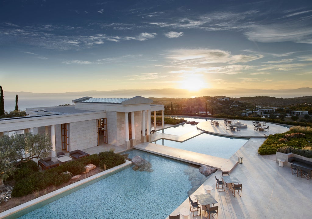 Elegant white pavilion with infinity pool overlooking Mediterranean Sea at sunset, featuring classical Greek columns and panoramic views