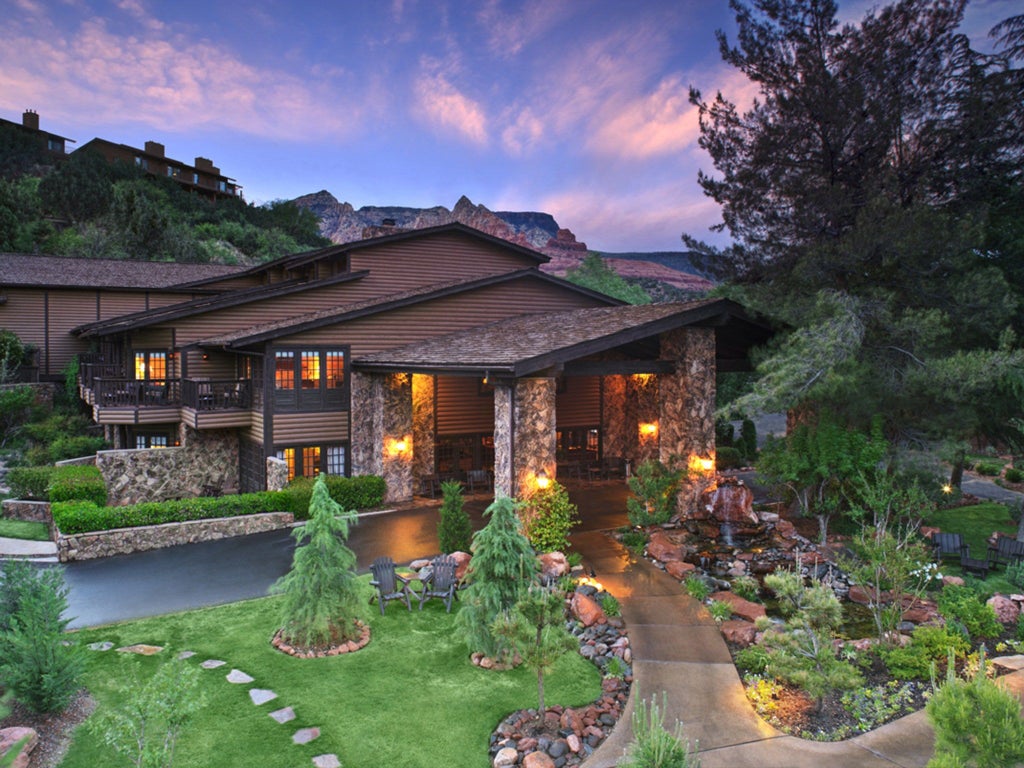 Elegant hotel facade with stone archways and flowering gardens, illuminated by warm evening lighting against a desert backdrop