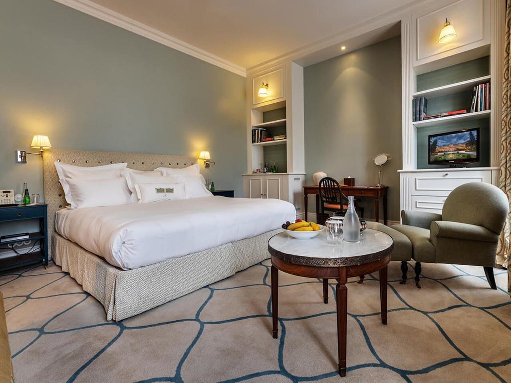 Elegant Portuguese luxury hotel room with plush white bedding, ornate crystal chandelier, and classic wood furnishings at Scenset Vidago Palace Hotel