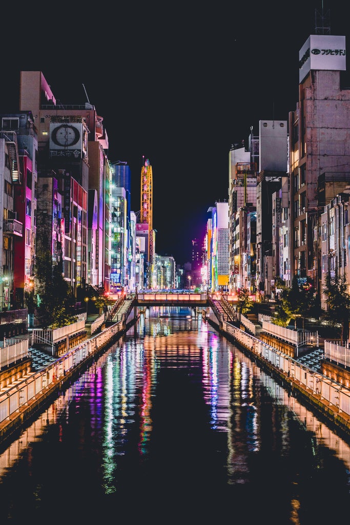 Sunset view of Osaka's iconic Dotombori district with glowing neon signs reflecting on canal waters, surrounded by modern skyscrapers