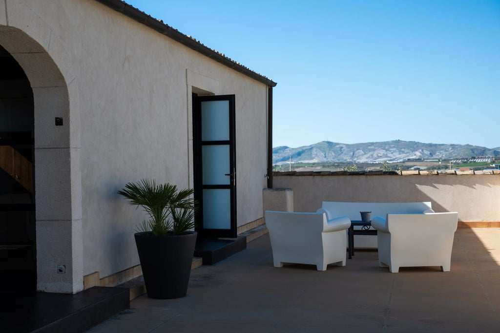 Elegant Sicilian suite with soft neutral tones, featuring a king-sized bed, wooden floors, and large windows overlooking scenic countryside landscape