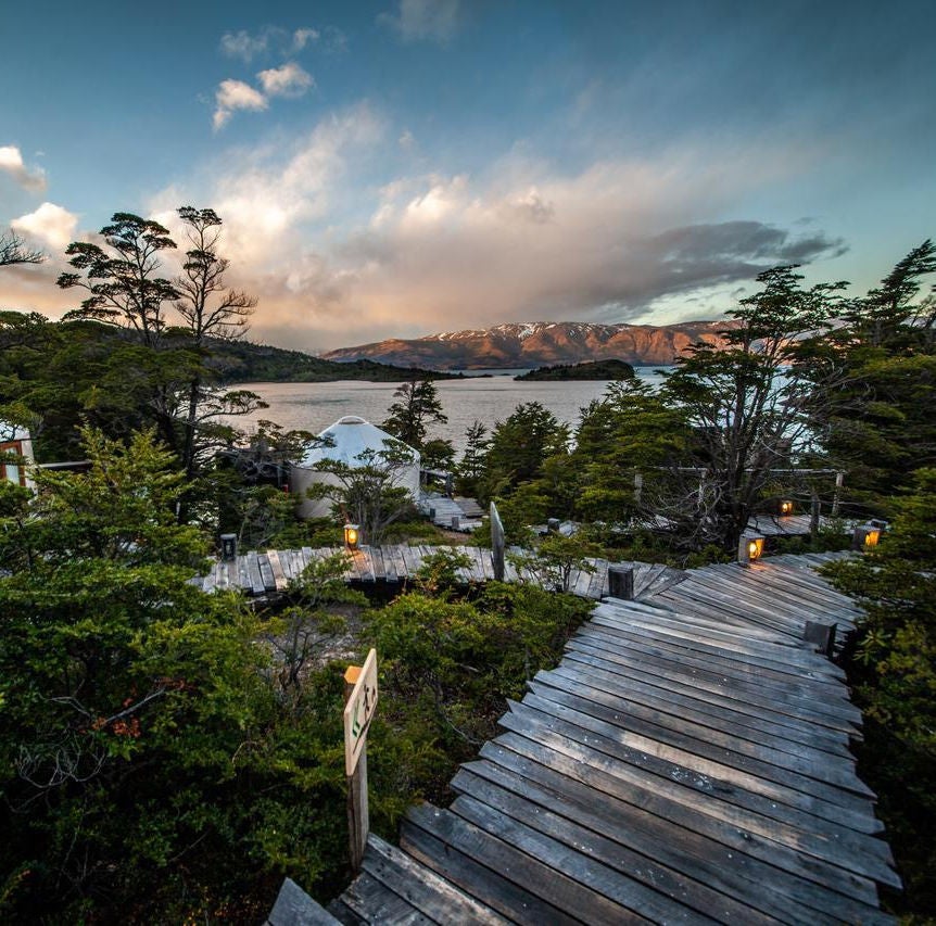 Luxurious geodesic dome tent perched on wooden platform overlooking pristine Patagonian lake and snow-capped mountain peaks at sunset