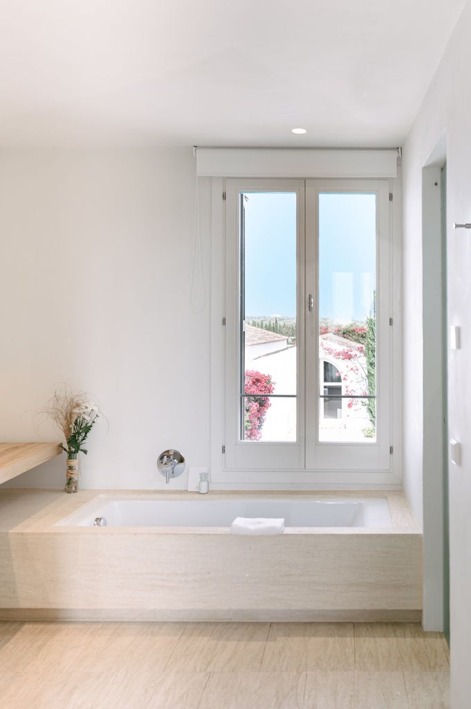 Elegant whitewashed Spanish villa bedroom with panoramic Mediterranean sea view, minimalist design, and stone tile flooring bathed in soft natural light