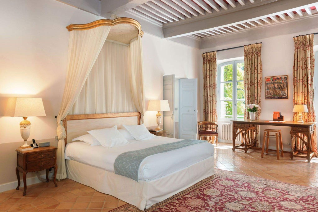 Elegant French country hotel room with antique furnishings, soft cream linens, rustic stone walls, and soft natural lighting in Provence