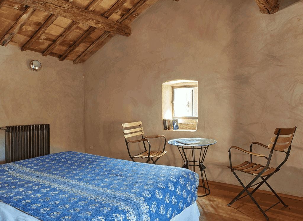 Elegant stone-walled bedroom in French countryside hotel with antique wooden furniture, soft linens, and rustic charm of traditional Provençal architecture