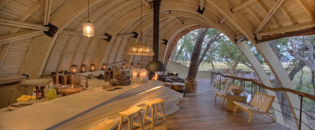 Elevated private safari lodge with wooden walkways and thatched pavilions nestled among palm trees overlooking Okavango Delta at sunset