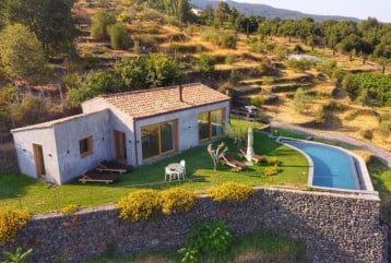 Elegant Sicilian countryside boutique hotel with restored stone building, lush vineyards, and Mount Etna backdrop at golden sunset