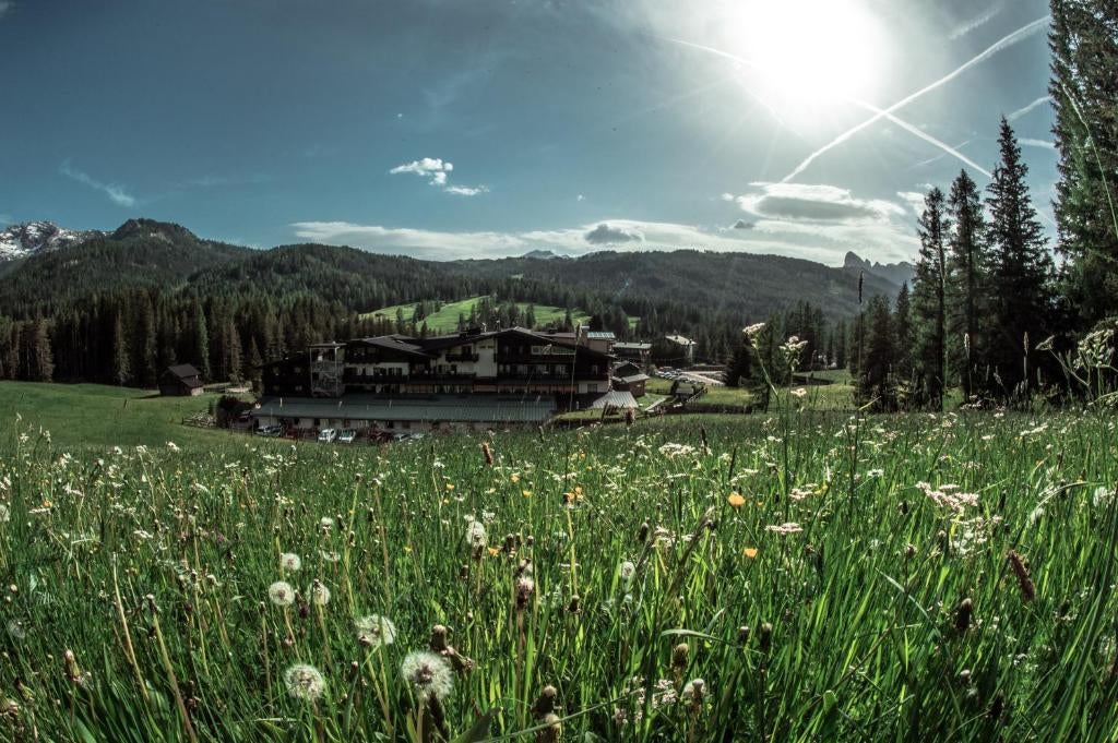 High-end Italian mountain lodge with rustic wood exterior, stone accents and snow-capped Dolomite peaks rising dramatically behind