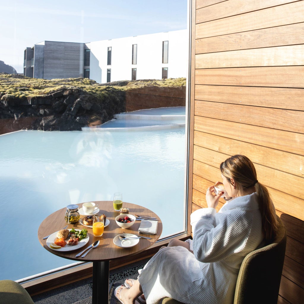 Luxurious minimalist hotel nestled against stark Icelandic landscape, featuring sleek wooden exterior and panoramic windows reflecting dramatic volcanic terrain