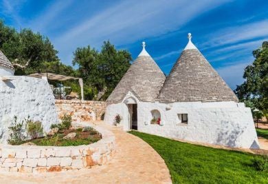 Rustic stone trulli houses with white-washed walls nestled in scenic Italian countryside, showcasing traditional Pugliese luxury architecture at scenic hotel.