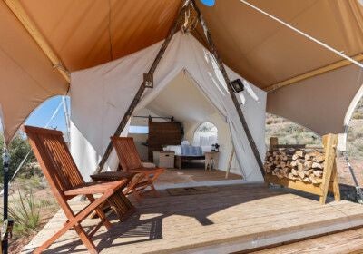 Luxurious safari-style canvas tent at Under Canvas Zion with king bed, large windows overlooking stunning red rock landscape at sunset