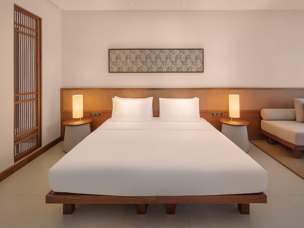 Spacious Deluxe Suite at Azerai Ke Ga Bay with ocean-view window, contemporary Vietnamese design, plush white bedding, and minimalist coastal elegance