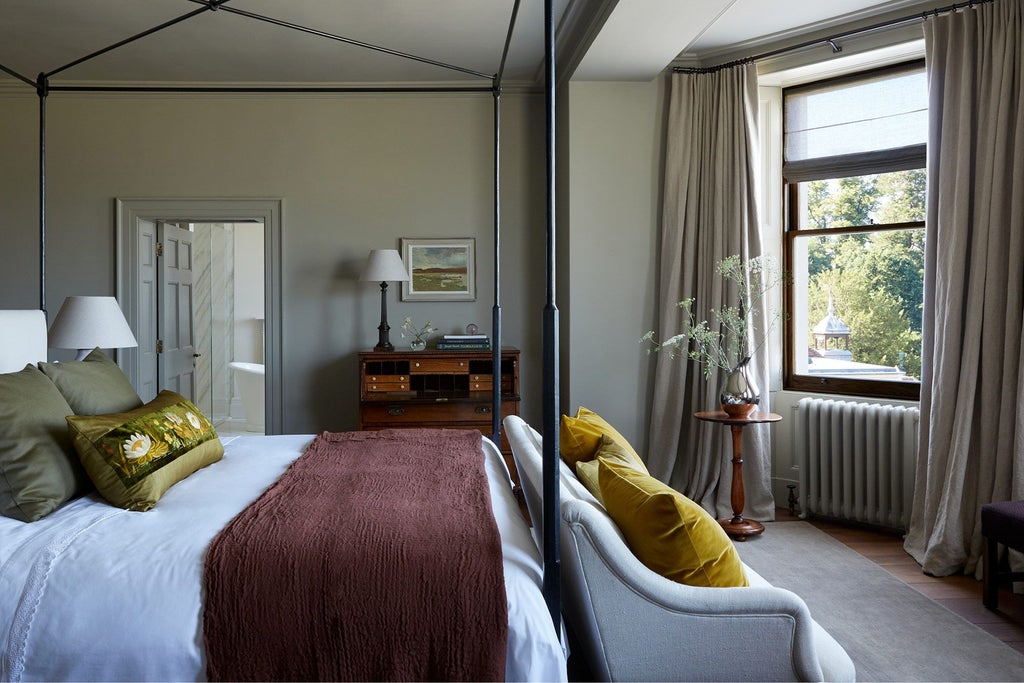 Elegant long hotel room with soft neutral tones, antique wooden furniture, plush armchairs, and expansive windows overlooking lush countryside at Heckfield Place