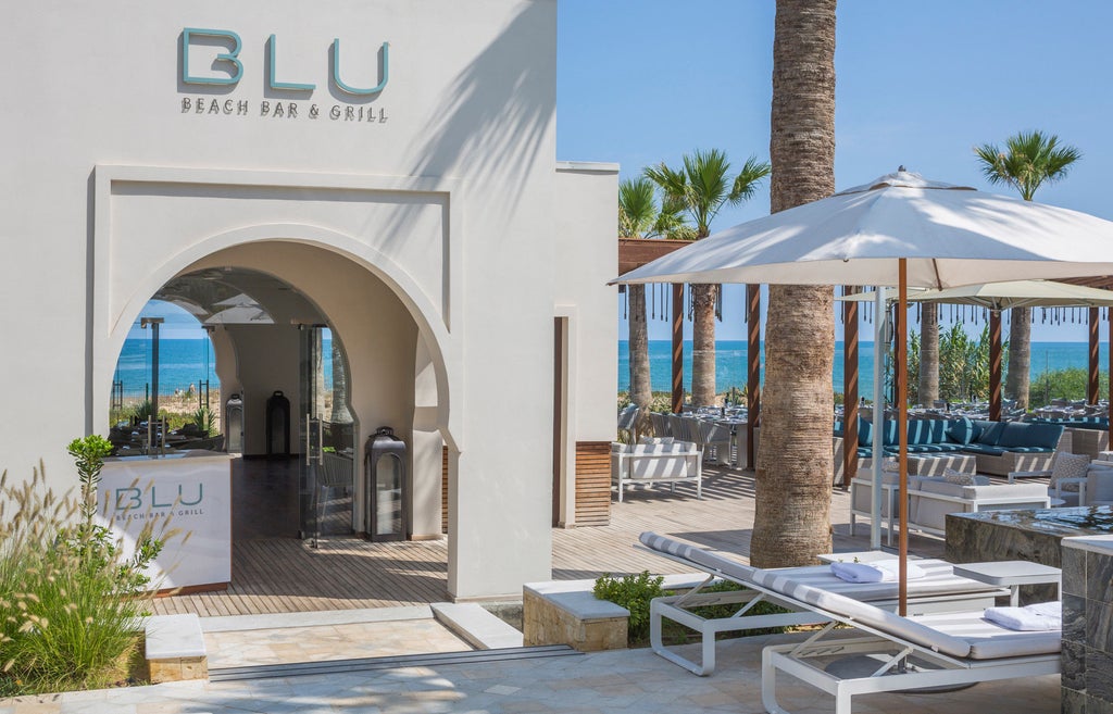 Elegant Mediterranean-style Four Seasons hotel with white facade, overlooking private beach, palm-lined pool and turquoise sea in Tunisia