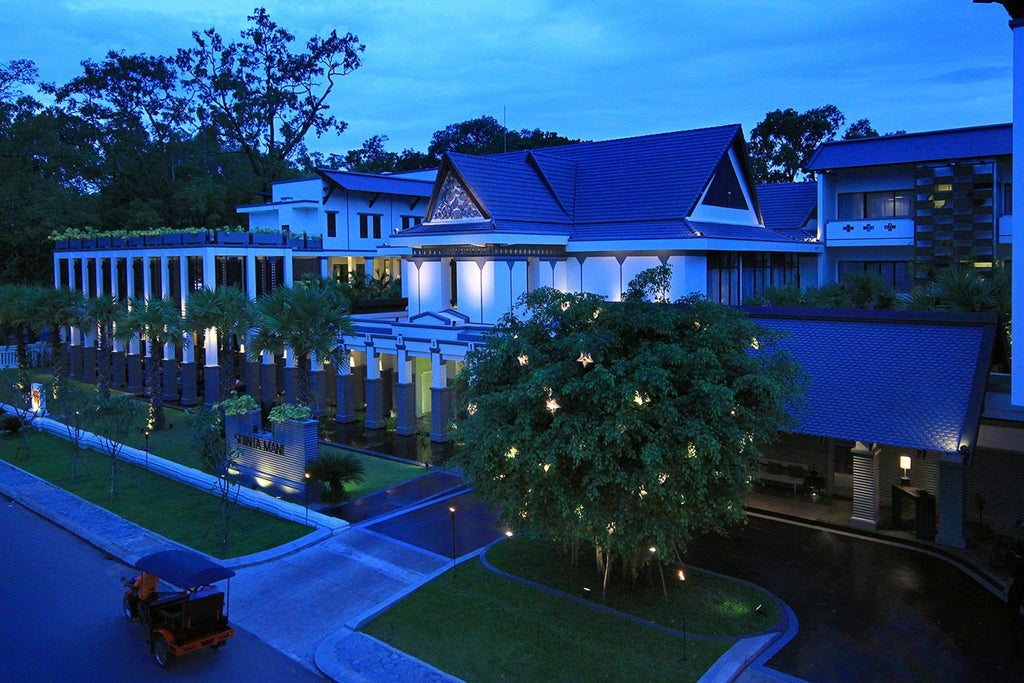 Elegant hotel entrance with stone pillars, reflecting pool, and manicured gardens set against modern Khmer-inspired architecture at dusk