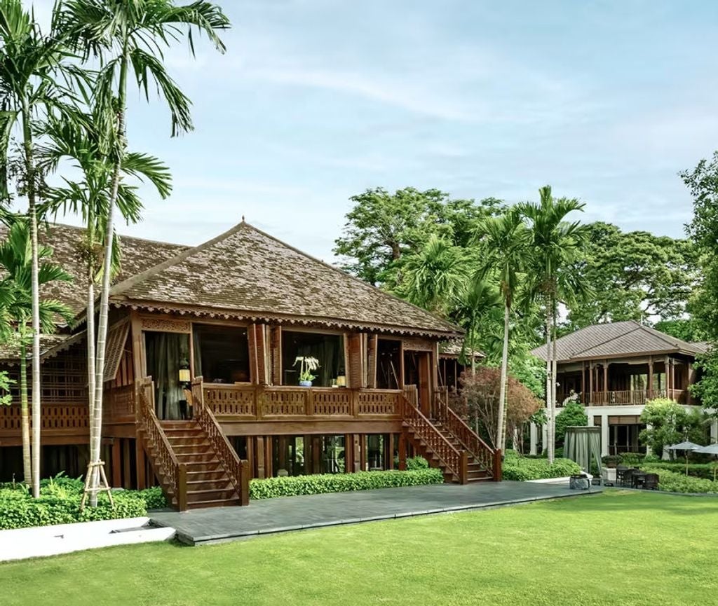 Colonial-style boutique hotel in Chiang Mai with white-pillared verandah, teakwood facade, and lush tropical gardens surrounding property