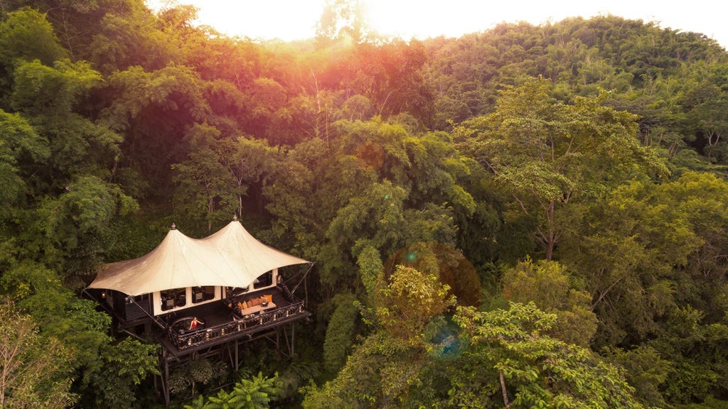 Luxury tent villa with private sundeck overlooking lush Thai jungle and mountains, featuring teak wood furnishings and outdoor seating