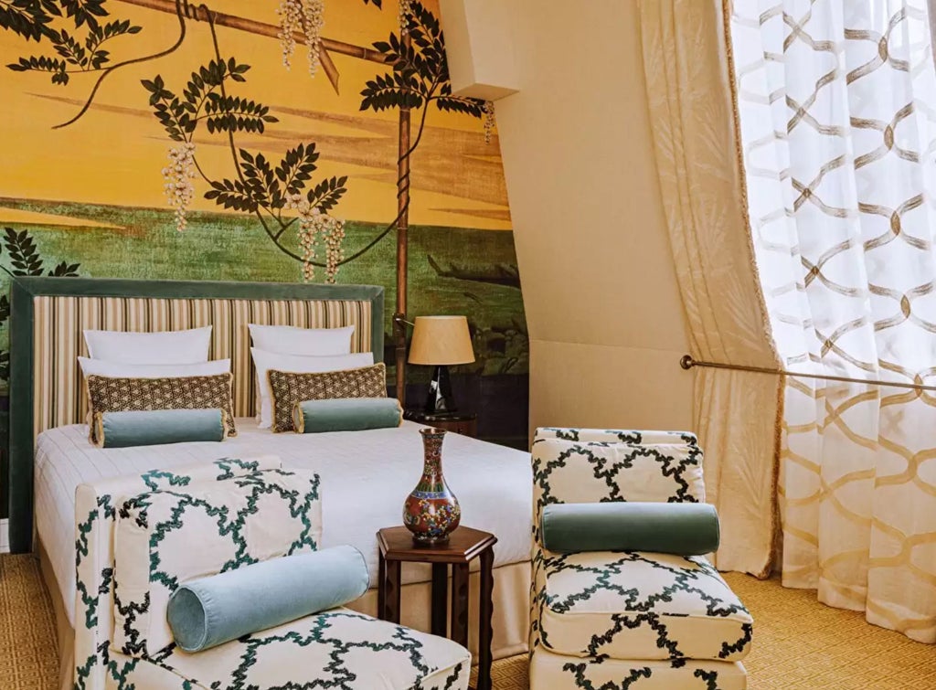 Elegant French hotel room with ornate gold-framed mirror, tufted velvet headboard, crystal chandelier and rich burgundy drapes by windows