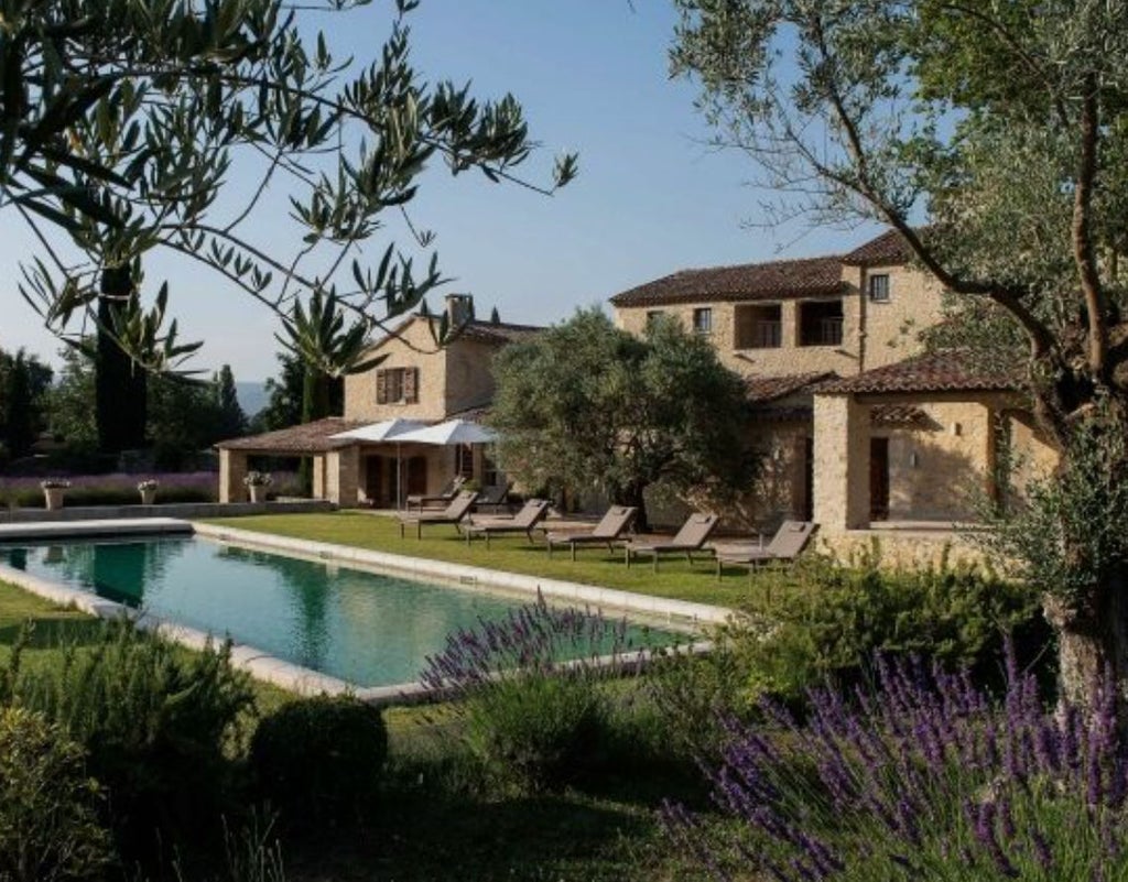 Elegant French hotel room with exposed stone walls, vaulted ceiling, luxurious bed linens, and Provençal-style furnishings bathed in warm light