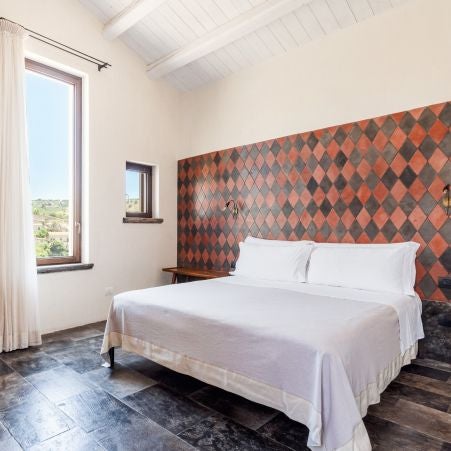 Elegant rustic bedroom in Casa Talía, Sciara, with stone walls, soft linens, and warm Mediterranean light filtering through traditional window.