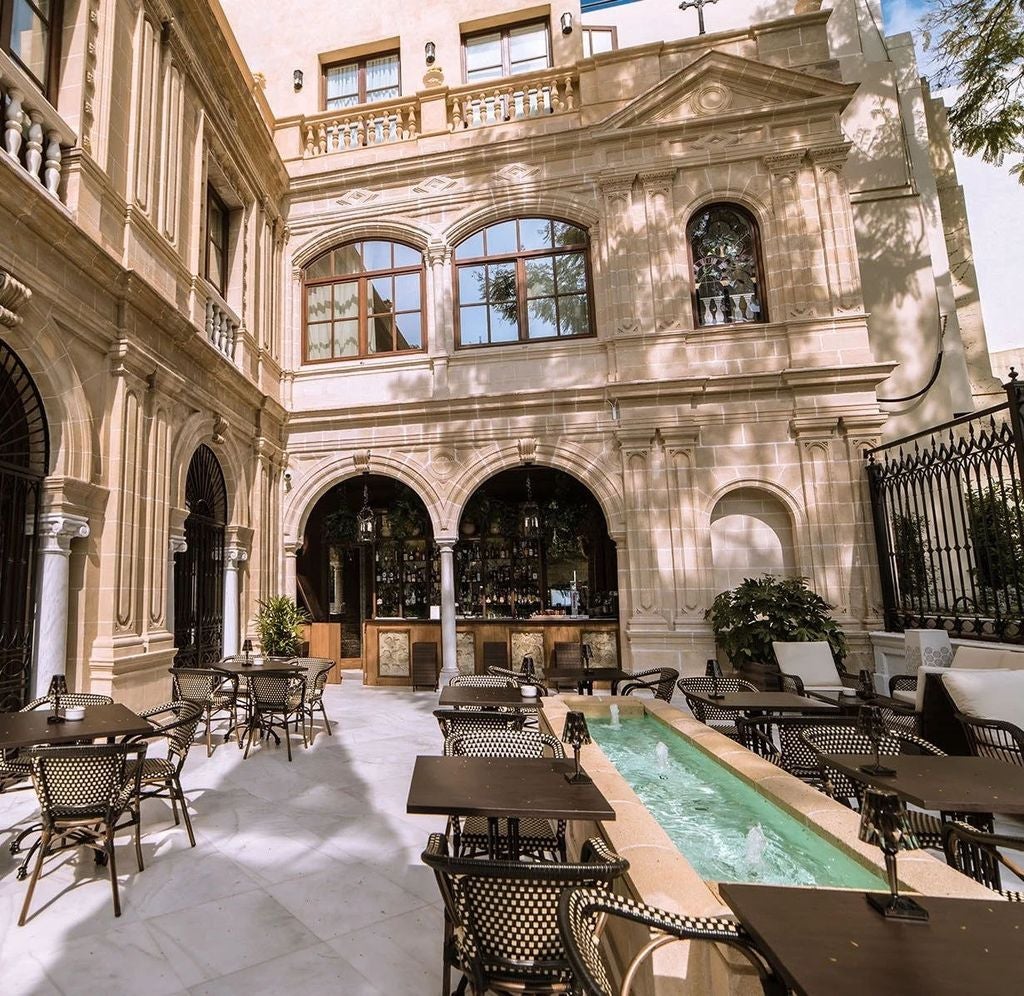 Ornate 19th century Spanish palace hotel featuring elegant white stone facade, arched windows, and wrought iron balconies in golden sunlight