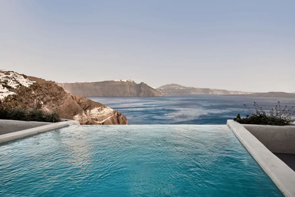 Cliffside luxury suite with private infinity pool overlooking Santorini's caldera, white cubist architecture against blue Aegean Sea