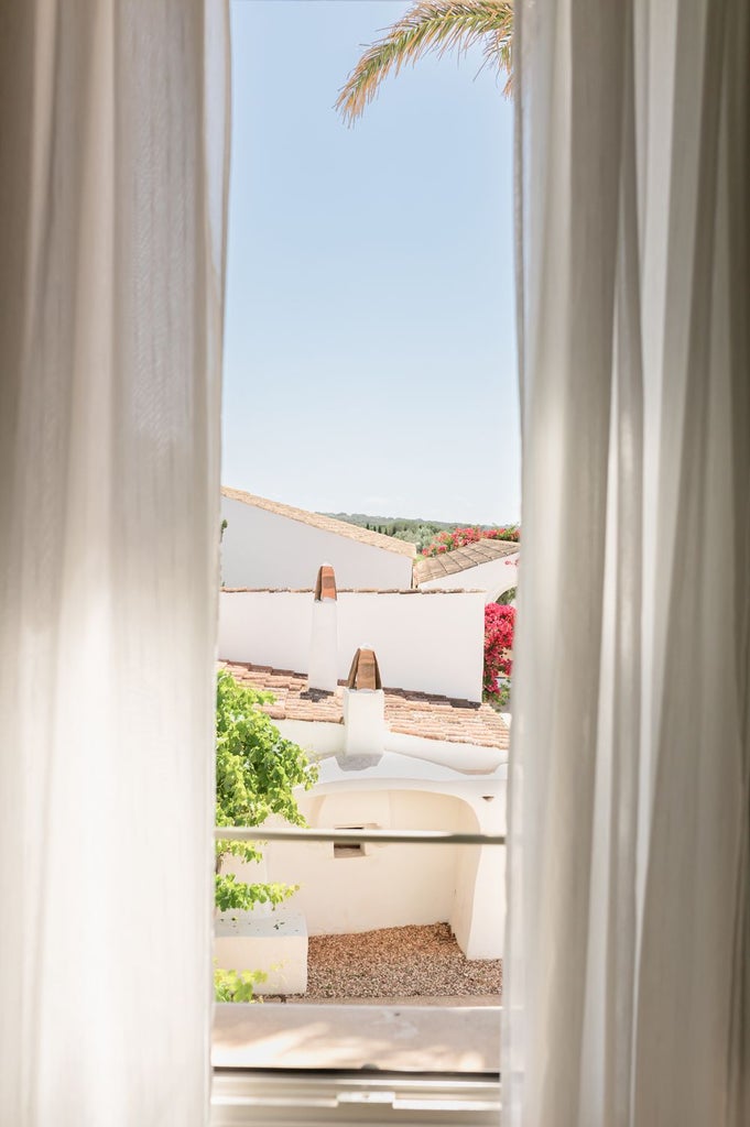 Elegant whitewashed Menorcan luxury hotel room with panoramic sea view, minimalist decor, and crisp linens overlooking Mediterranean coastline landscape