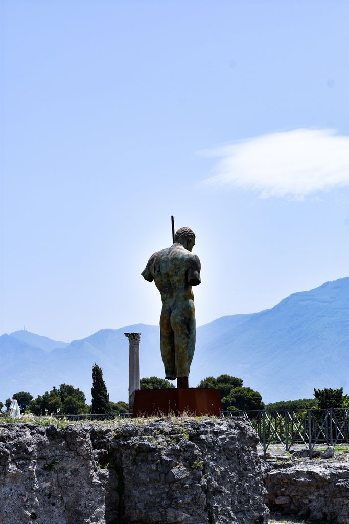 Ancient stone ruins of Pompeii's archeological site with Mount Vesuvius volcano looming in background under dramatic cloudy sky