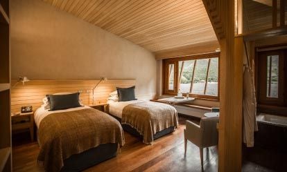 Spacious Peruvian hotel room with minimalist design, natural wood accents, crisp white linens, and panoramic mountain views of the Sacred Valley landscape