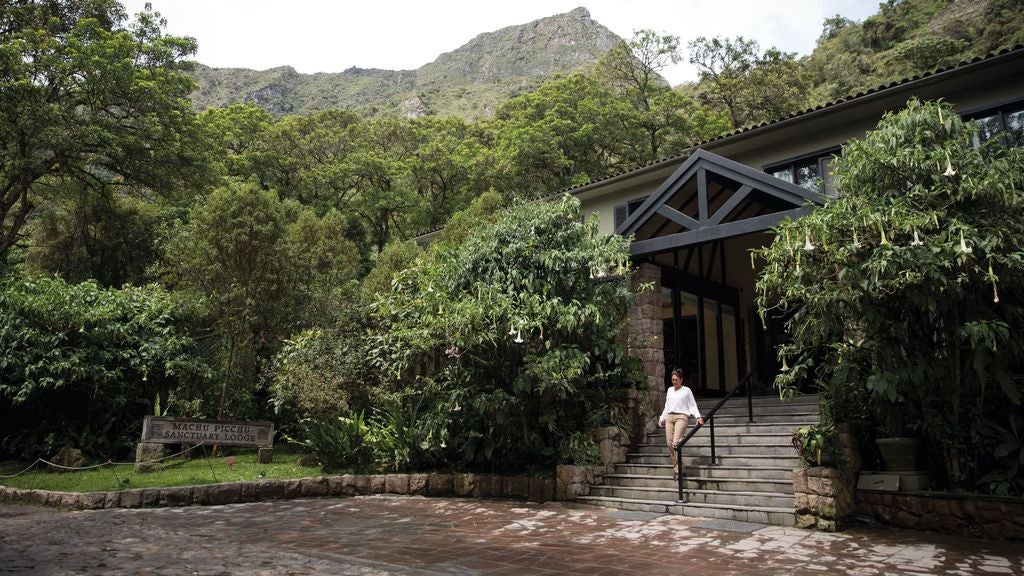 Majestic stone hotel nestled in misty Peruvian mountains with lush gardens, elegant archways, and traditional Andean architecture at sunset