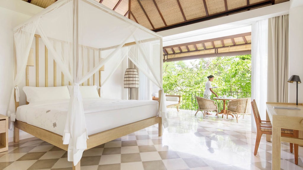 Elegant Balinese hotel room with four-poster bed, wooden furnishings, white linens, and natural light flowing through sheer curtains