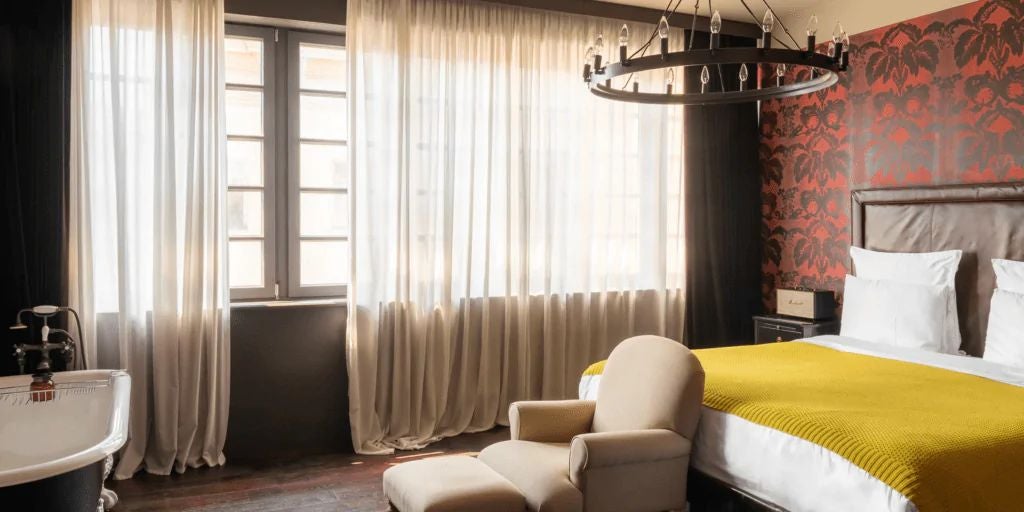 Luxurious Signature King room with modern design, featuring sleek gray furnishings, plush bed, and large windows overlooking urban Tbilisi landscape