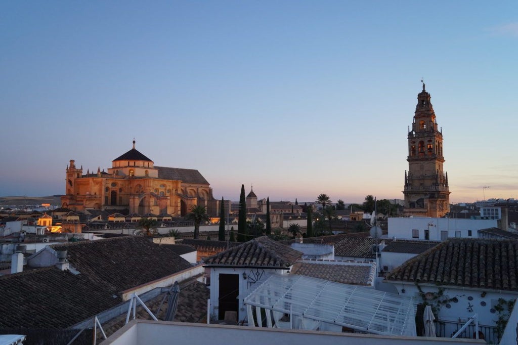 Elegant white-washed historic Spanish hotel with ornate balconies overlooking Córdoba's charming streets, featuring traditional Andalusian architectural details and warm sunlight