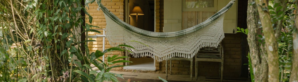 Elegant Brazilian coastal suite with warm wooden floors, crisp white linens, tropical decor, and large windows overlooking lush greenery in Trancoso