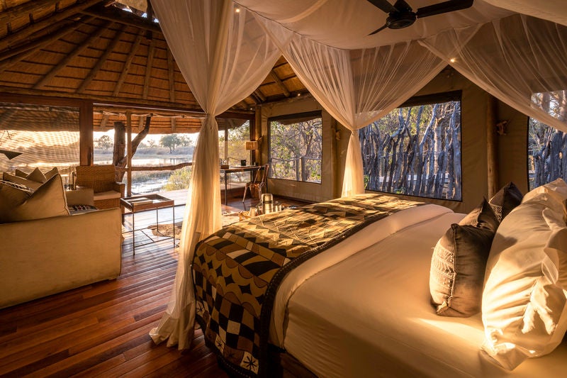 Elevated luxury safari camp overlooking Savuti Channel with canvas tents, wooden decks, and natural savanna landscape at sunset