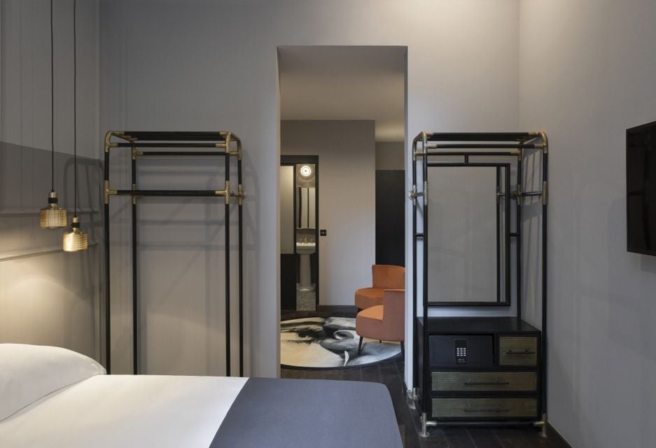 Luxurious loft-style hotel room at Chapter Roma with exposed brick walls, modern minimalist design, and sleek king-sized bed overlooking urban Italian cityscape