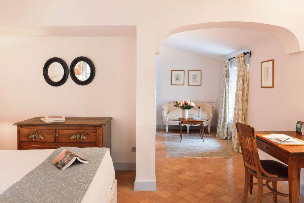 Elegant French hotel room with soft cream walls, antique furnishings, plush white bedding, and rustic stone architectural details in Provence