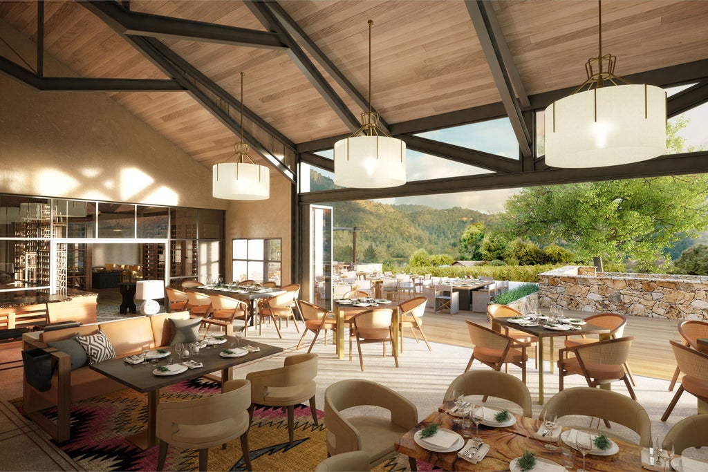 Modern luxury hotel building with stone facade, set against rolling Napa Valley vineyards and distant mountains at golden hour